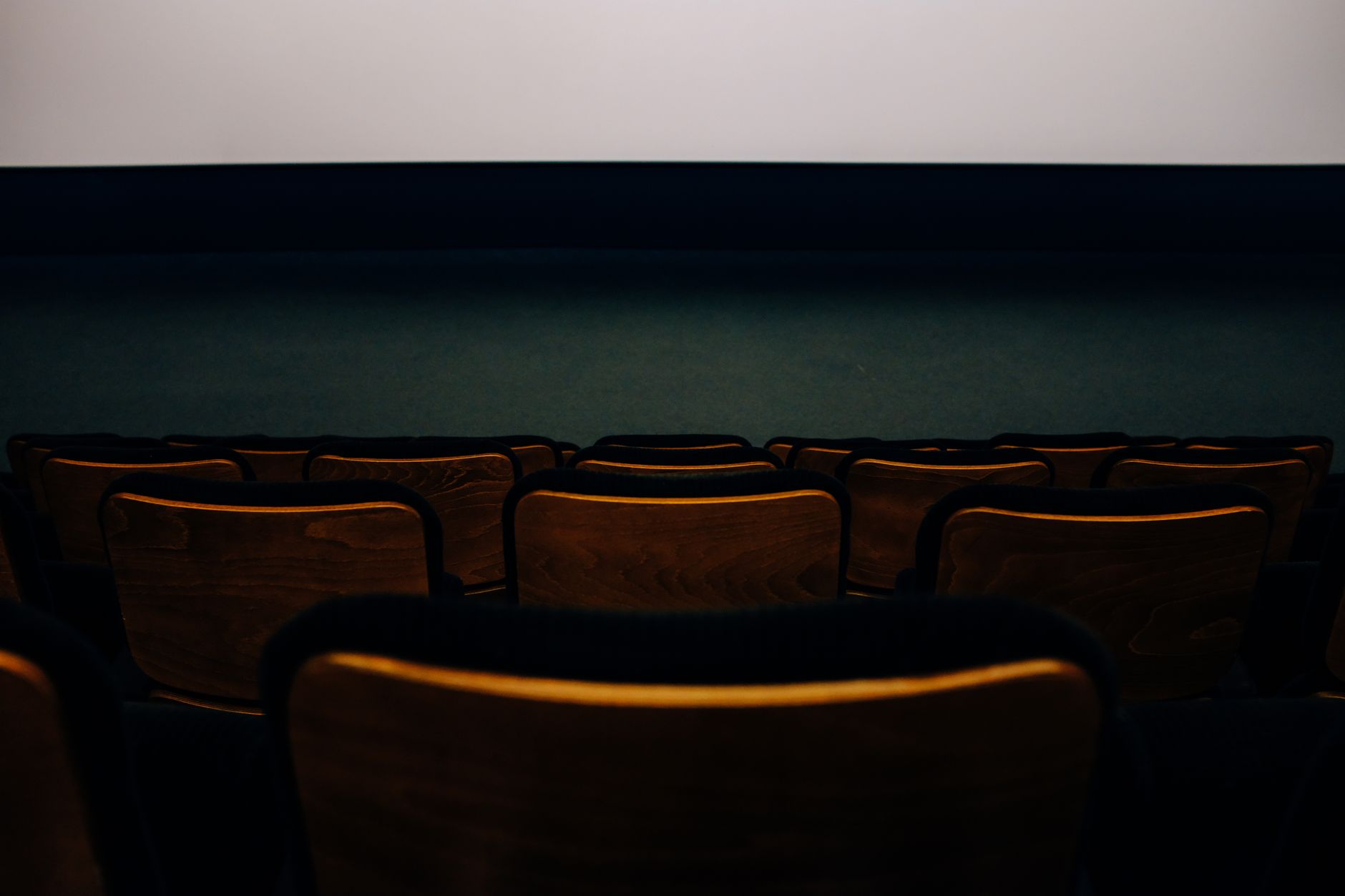 O sală de cinema goală, cu scaune de lemn în penumbră, întoarse spre un ecran alb